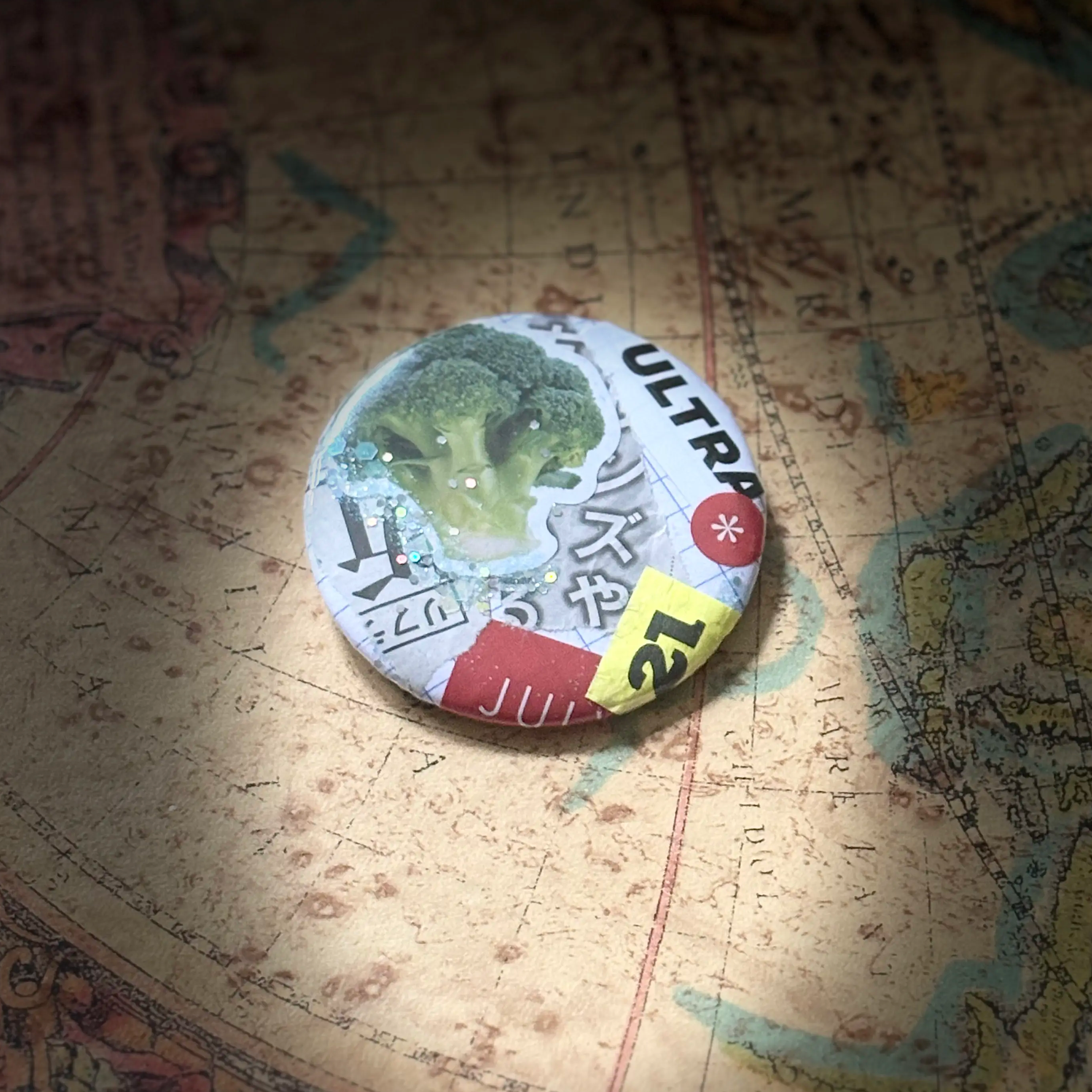 Round collage pin featuring a broccoli sticker, Japanese print, and mixed paper fragments