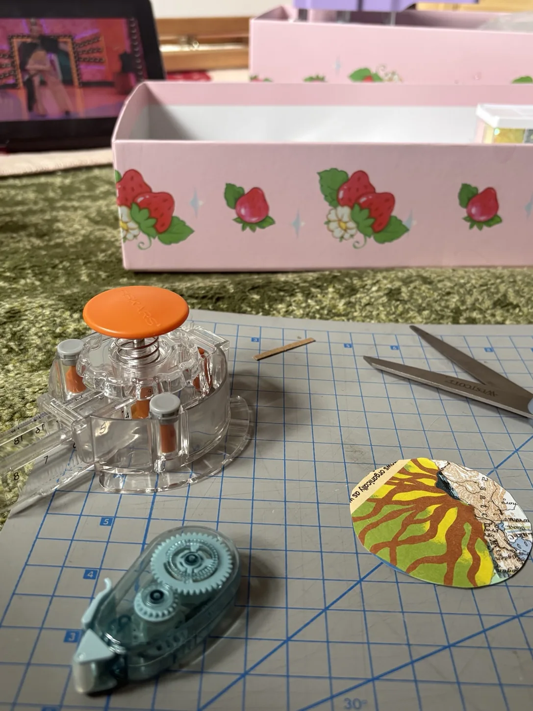 A circular paper collage in progress beside scissors and craft tools